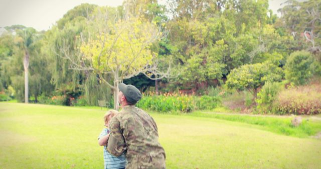 A middle-aged man in military attire is embracing a young child in a lush park, with copy space. Their affectionate hug conveys a touching reunion or farewell, related to military service.