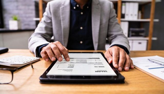 Male professional reviewing digital invoice on tablet at office desk with calculator