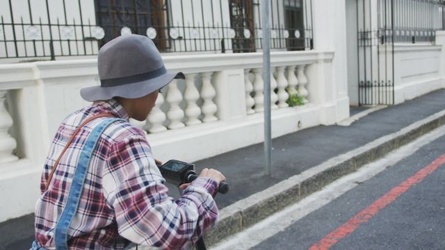 Image depicts a woman wearing a hat, riding an electric scooter along an urban street. This scene offers a sense of freedom and modern lifestyle, capturing a blend of sustainability and convenience in transportation. Useful for advertising urban mobility solutions, environmental commuting options, or promoting brands emphasizing space-saving and eco-friendly vehicle alternatives.