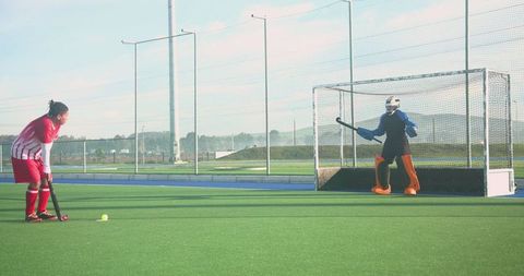 Teen Field Hockey Player in Red Taking a Strike at the Goal on Sunny Day