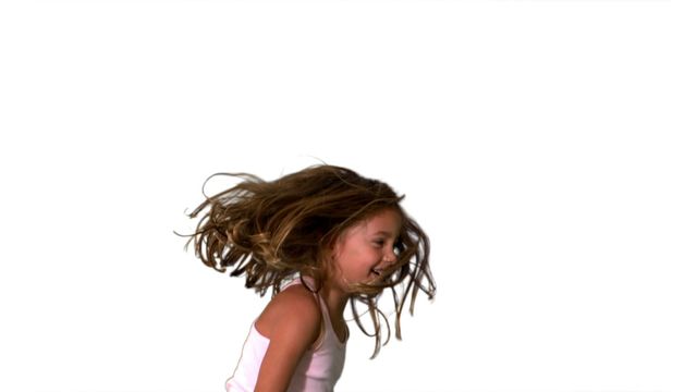 Young girl energetically jumping and turning playfully with toy in hand against plain white background. Ideal for use in advertisements, educational materials, and promotions emphasizing joy, childhood innocence, and carefree fun.