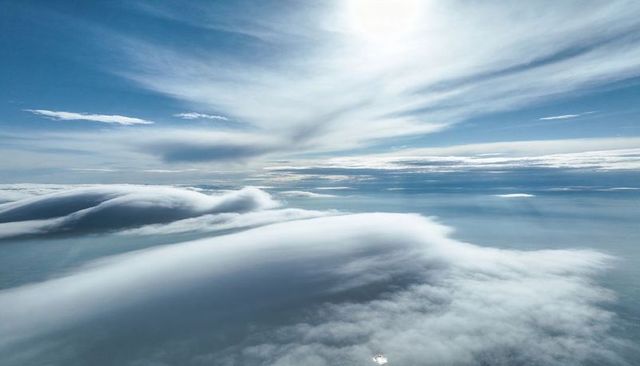 Layered Clouds Flowing Over Ocean at High Altitude Under Sunlit Cirrus Streaks
