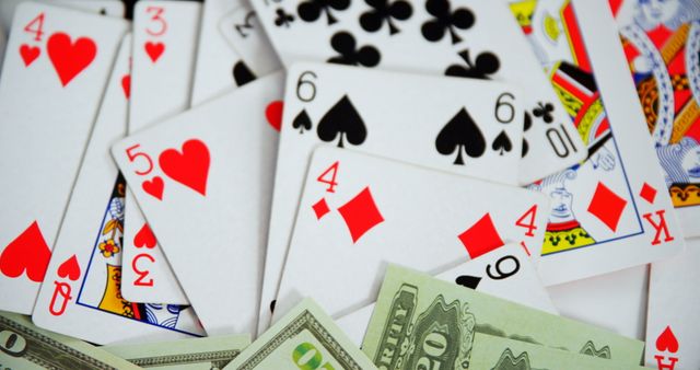 Close-up showcasing playing cards scattered alongside US dollar bills, representing gambling and casino themes. Useful for illustrating financial risk, gaming, and entertainment in promotional materials, advertisements, and editorial pieces.