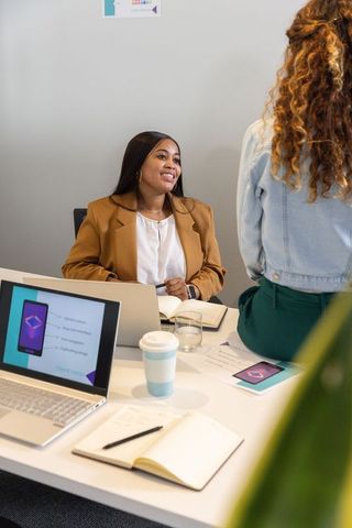 Smiling manager leading diverse team meeting around laptop with notebooks and coffee