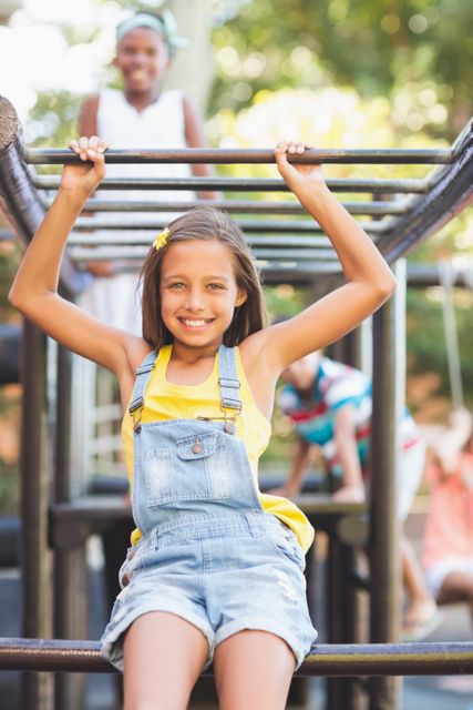 Happy schoolgirl sitting on monkey rack at playground