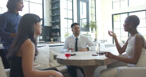 African american friends gathering around round wooden table in bright modern kitchen