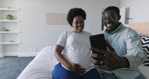 African American Expecting Couple Smiling and Taking Selfie on Bed, Pregnancy Joy at Home