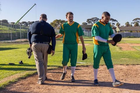 Baseball players and umpire walking off infield after disputed call in green uniforms