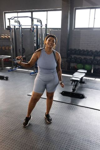 Smiling woman holding resistance band in sunlit industrial gym wearing blue activewear