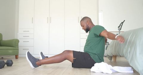 Man exercising at home on bedroom floor stretching after dumbbell workout with towel nearby