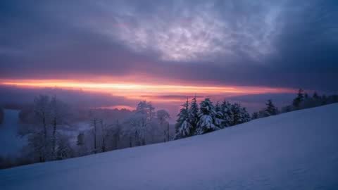 Recording sunrise over snowy hillside with fog rolling and horizon glow widening