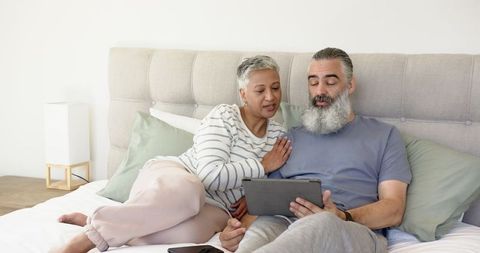 Senior Couple Relaxing in Cozy Bedroom with Tablet and Smartphone