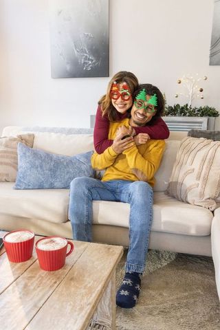 Couple hugging on couch wearing festive novelty glasses enjoying holiday cocoa