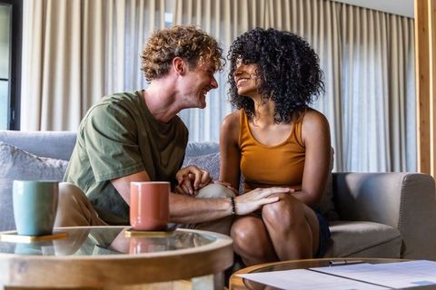 Couple laughing and holding hands on sofa, cozy living room romance moment