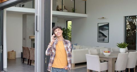Young Man Relaxing at Modern Home while On Phone Call by Sliding Glass Door