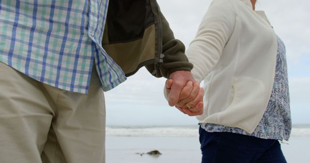 Midsection of senior caucasian couple holding hands on beach. Retirement, summer, leisure, vacation and senior lifestyle.