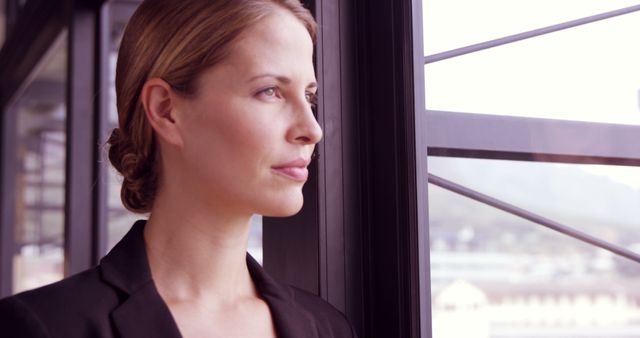 Confident Professional Woman Near Office Window with Contemplative Expression - Download Free Stock Images Pikwizard.com