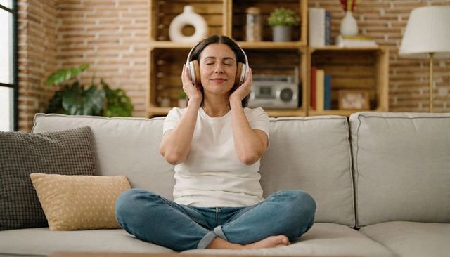 Woman listening to music on cozy sofa wearing headphones, enjoying relaxing home moment
