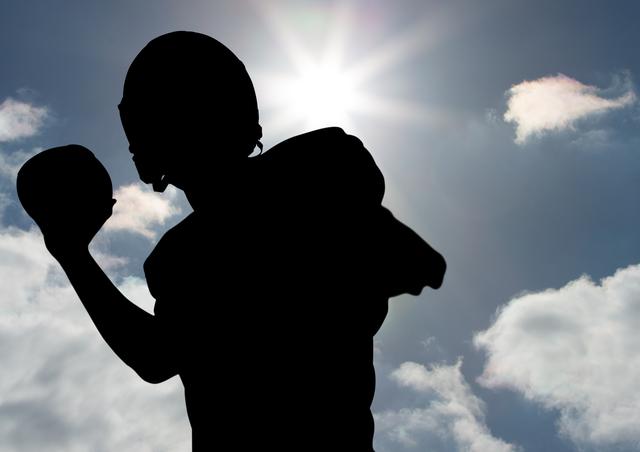 Silhouette of player throwing a ball against sunny sky in background