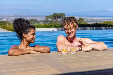 Relaxing couple at infinity pool, sipping lemon drinks, enjoying mountain and city view