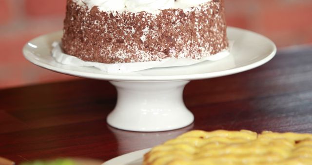 A delicious-looking chocolate cake topped with white frosting sits on a white cake stand, ready to be served. Its tempting appearance makes it a perfect centerpiece for a dessert table or a celebration.