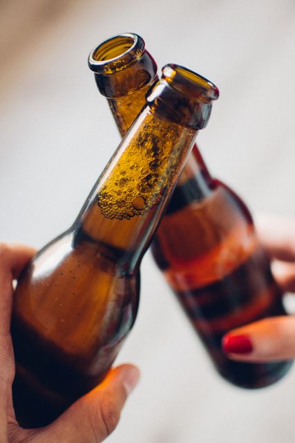 Two people clinking beer bottles in a cheerful manner. Suitable for use in social gatherings, celebration, and friendship-themed designs, advertisements, or articles.