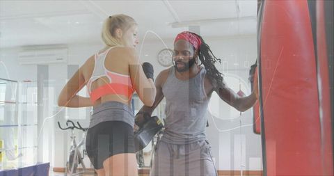 Boxing coach guiding female trainee punching heavy bag during focused one-on-one training