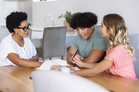 Diverse couple consulting financial advisor at home signing documents on wooden table