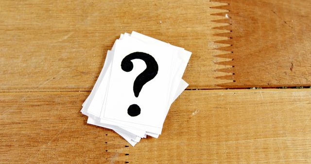A stack of white cards with a black question mark is placed on a wooden surface, with copy space. It symbolizes inquiry, curiosity, or the concept of unanswered questions and mystery.