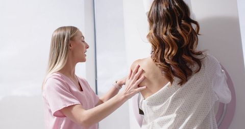 Clinician positioning patient for mammogram screening in modern bright radiology clinic