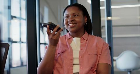 African professional speaking into smartphone during modern office meeting