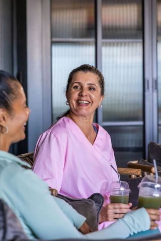 Smiling diverse female healthcare coworkers in pink scrubs chatting over green smoothies
