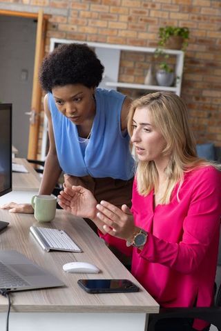 Diverse Female Coworkers Collaborating Over Computer in Modern Office