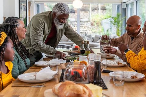 Multigenerational black family sharing meal and serving bread in sunlit rustic dining room
