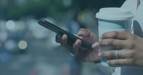 Woman Using Smartphone while Holding Coffee Cup in Urban Setting