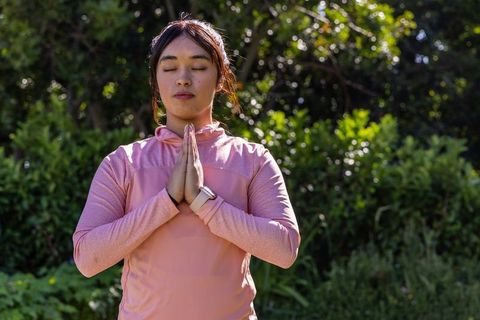 Asian woman practicing mindfulness outdoors pressing palms to chest wearing smartwatch