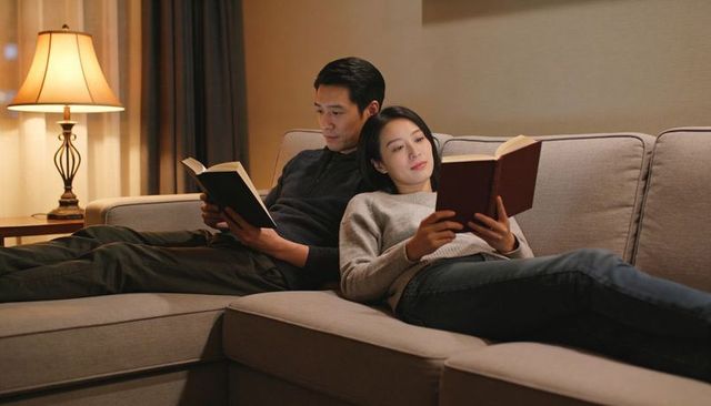 Asian couple relaxing on sofa reading books together evening cozy home moment