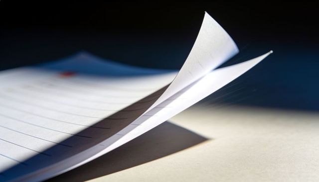 Wide-ruled notebook paper curling at top corner with dramatic light, shadow and texture