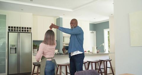 Diverse Couple Dancing While Cooking at Bright Modern Kitchen Island with Barstools