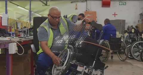Wheelchair Technician Assembling Mobility Chair in Workshop Wearing Hi-Vis Vest and Safety Glasses