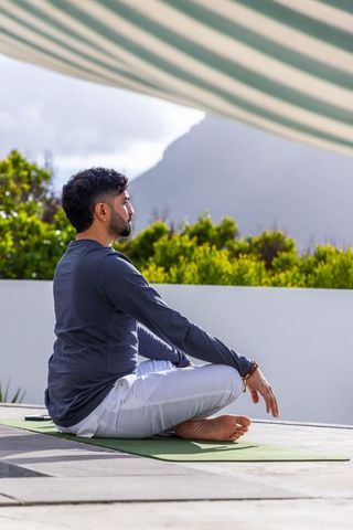 Man sitting cross-legged on rooftop terrace meditating with mountain view and sunshade