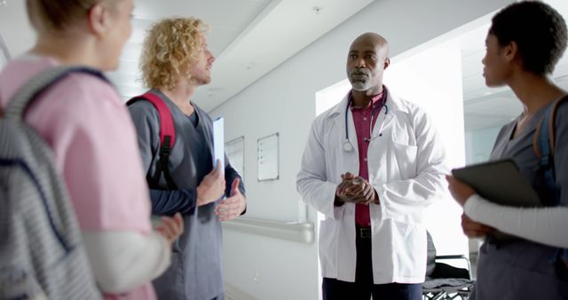 Doctor briefing group of medical students during learning session in hospital hallway. Could be used for illustrating medical education, healthcare practices, and professional training.