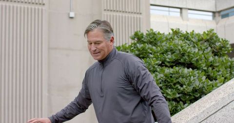 Mature man descending concrete steps steadying with arm in urban plaza