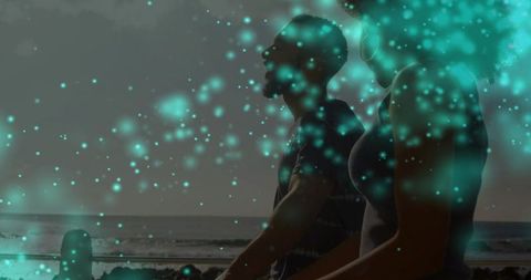 Silhouetted couple watching ocean at dusk with teal bokeh light overlay