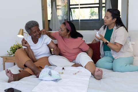 Multigenerational african american women sharing led skincare ritual on sunlit bed