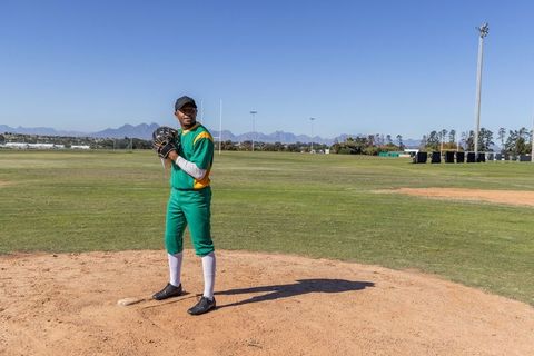 African American pitcher standing on mound in green and yellow uniform with glove