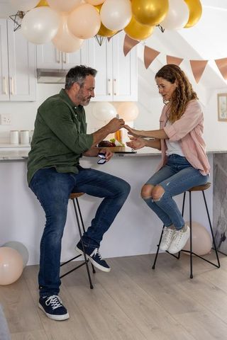 Couple celebrating engagement as man proposing on kitchen island with balloons and banner