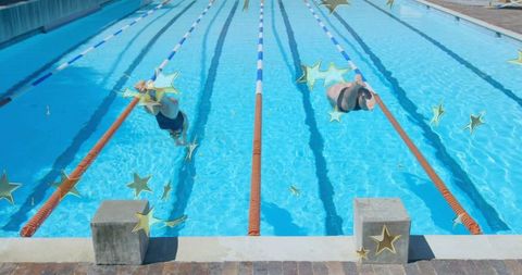 Two swimmers diving headfirst into outdoor lap pool from starting blocks