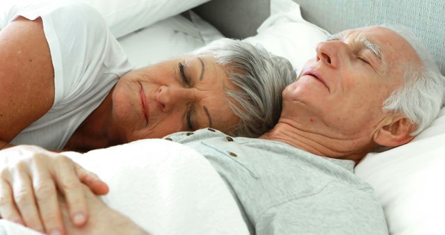 Senior man and woman peacefully sleeping together in bed, symbolizing comfort, love, and relaxation. This image can be used to promote healthy aging, retirement living, or sleep-related products and services.