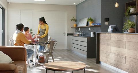 Diverse barista serving coffee to customers in sunlit modern cafe with wood counter